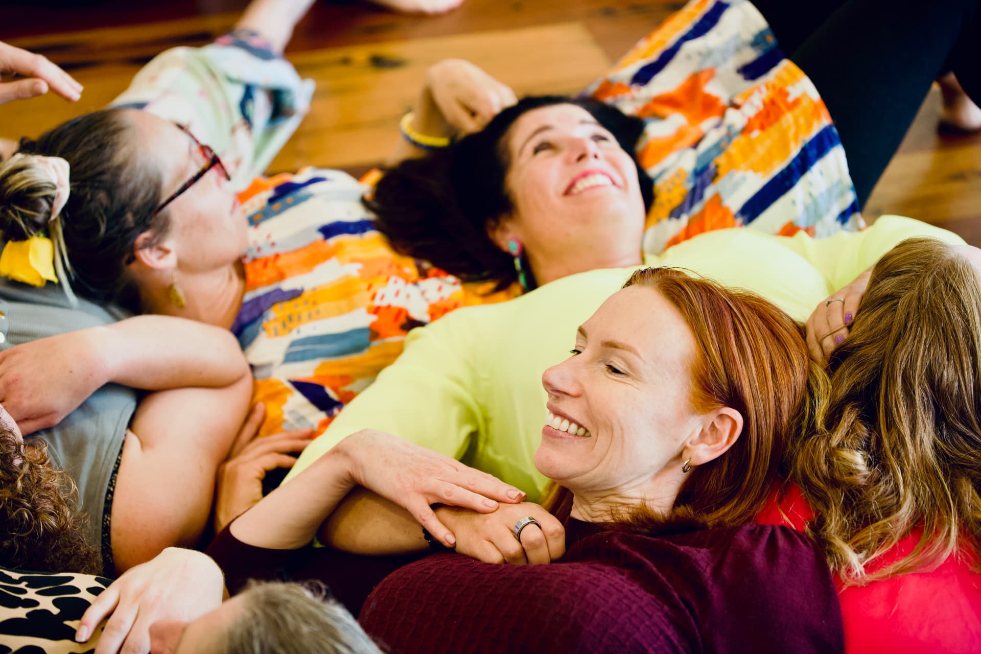 Women lying on the wooden floor laughing together during a retreat exercise